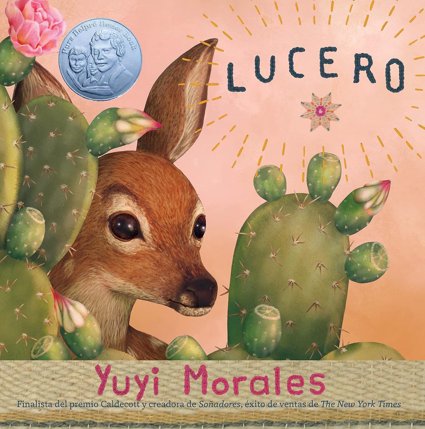 Illustration of a fawn peeking through cacti under a pink sky, symbolizing growth. The title Lucero is at the top with a silver medal emblem. Celebrated author Yuyi Moraless name appears below, accompanied by a Spanish description.