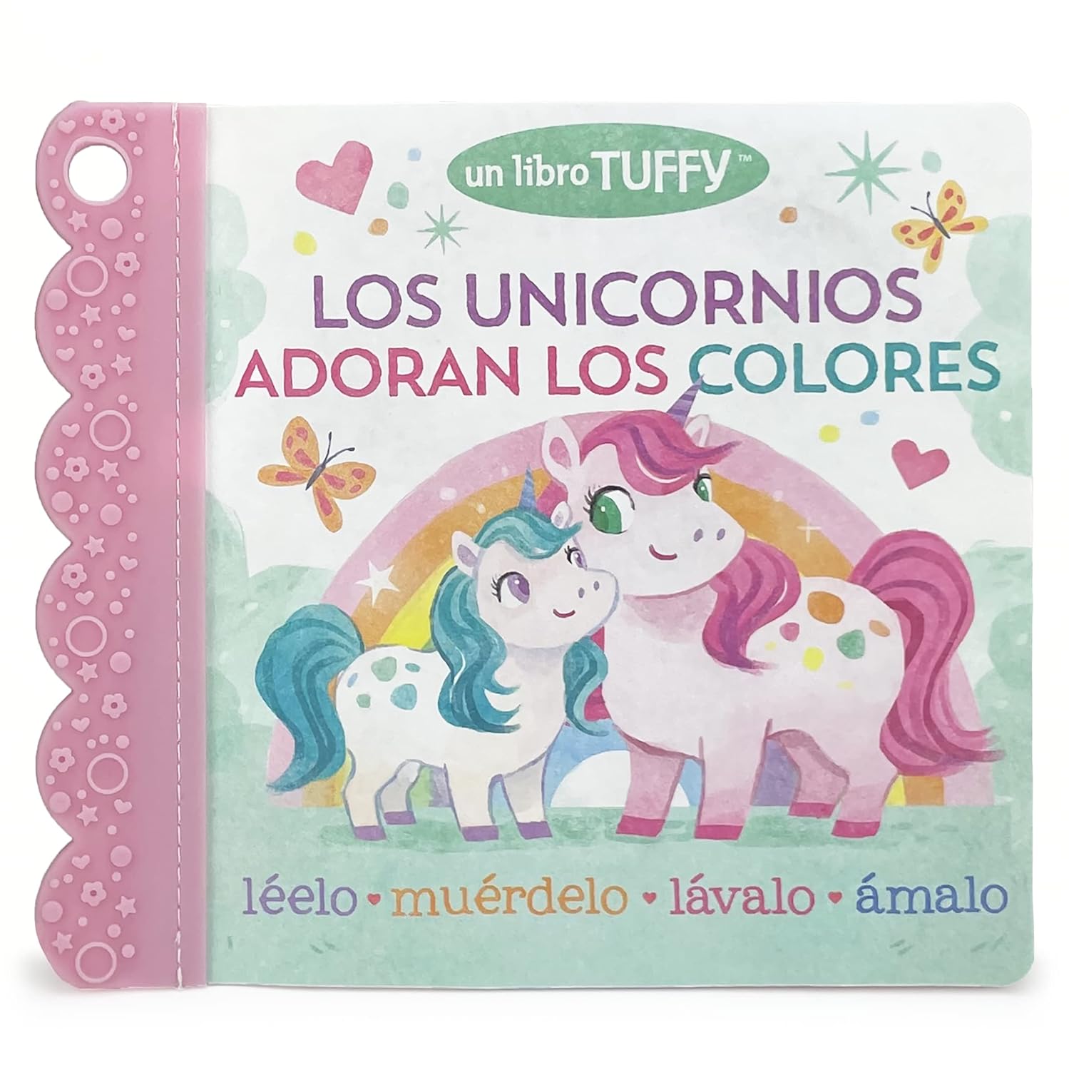 The image displays the cover of Los Unicornios Adoran Los Colores, a childrens book with two cartoon unicorns—one pink and one white with green hair—amidst butterflies. The Tuffy book has a textured pink spine, ideal for little hands, resembling a teether book.
