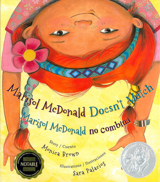 The Marisol McDonald Doesnt Match book cover features a red-haired girl with a pink flower in her hair, wearing a colorful outfit representing her Peruvian-Scottish roots. The title is bilingual, displayed in English and Spanish, with a silver medal at the bottom right.