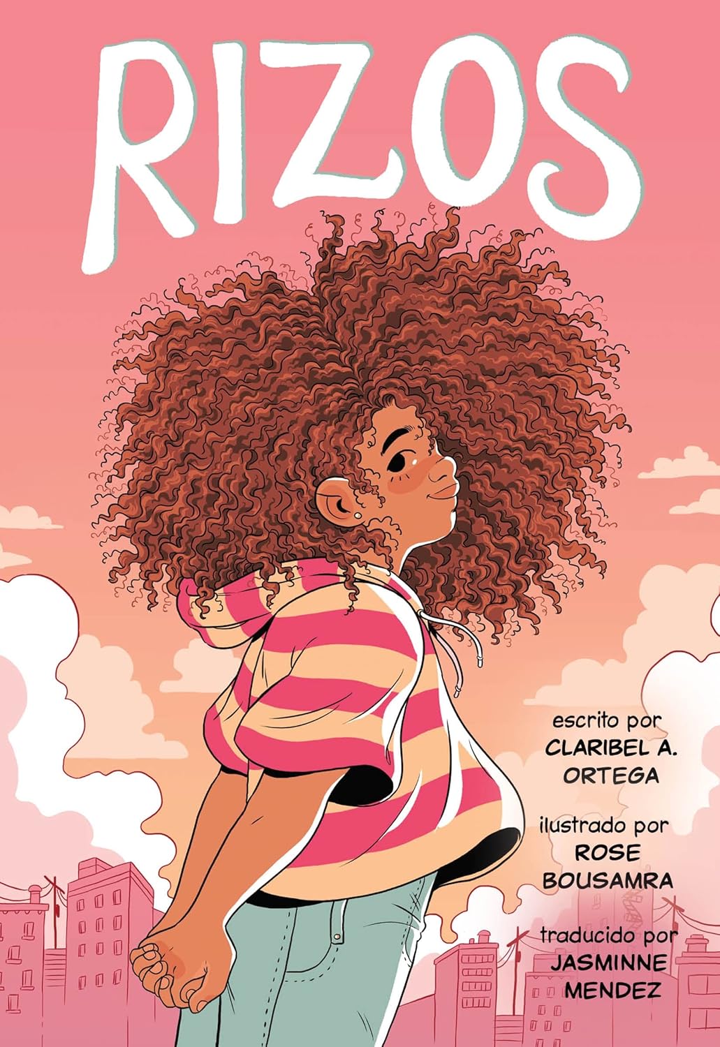 The cover shows a young girl with curls against a pink sky and skyline, wearing a striped shirt. Text reads: Rizos, by Claribel A. Ortega, Rose Bousamra, and Jasmine Mendez—a middle-grade graphic novel on self-acceptance. Product name: Rizos (Spanish Edition).